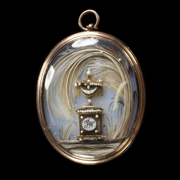 Żałobny medalion z 1775–1800 r., wykonany ze złota, ozdobiony kryształem przykrywającym kompozycję wykonaną z włosów, metalu oraz maleńkich pereł osadzonych na opalizowanym szkle pomalowanym akwarelą. Stylizowana urna ozdobiona została inicjałami FW; ©Victoria & Albert Museum, London