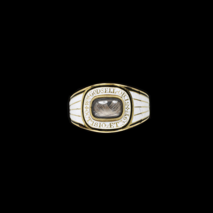 Pierścień żałobny z 1810 r., wykonany ze złota, ozdobiony prostokątnym kryształem z plecionymi włosami, czarną oraz białą emalią. Na obrączce umieszczono napis: „W M GODSELL. OB: 12.OCT: 1810 AET: 39 YS”; ©Victoria & Albert Museum, London