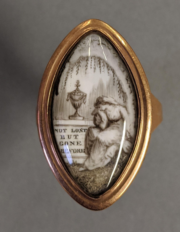 Pierścień żałobny z końca XVIII w., wykonany ze złota, ozdobiony miniaturą przedstawiającą kobietę siedzącą przy urnie ustawionej na postumencie z napisem: „NOT.LOST.BUT.GONE.BEFORE” oraz inskrypcją na wewnętrznej stronie: „Ann Scurfield Ob 20 Octr 1790 Aet 59”; ©Victoria & Albert Museum, London
